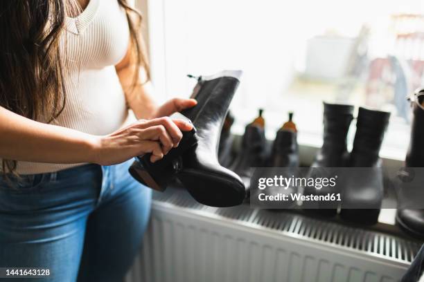 woman polishing boot standing by window at home - polishing shoes stock pictures, royalty-free photos & images
