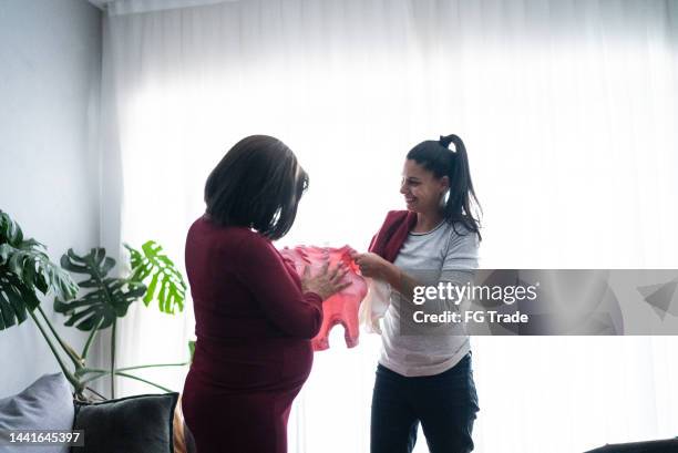 pregnant lesbian couple looking a baby clothing in the living room at home - baby clothes stock pictures, royalty-free photos & images