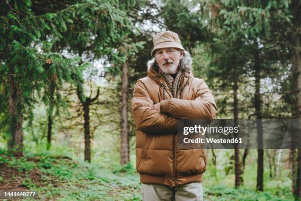 senior man standing with arms crossed in forest - bucket hat stock pictures, royalty-free photos & images