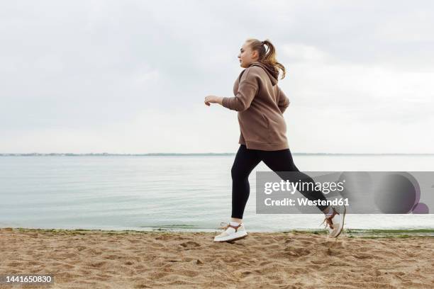 young woman jogging on beach - dicke frauen am strand stock-fotos und bilder