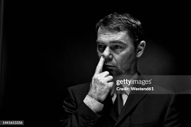 mature man putting finger in nose against black background - picarse la nariz fotografías e imágenes de stock