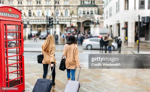 uk, london, two friends exploring the city, arriving with trolley bags - london phone booth stock pictures, royalty-free photos & images
