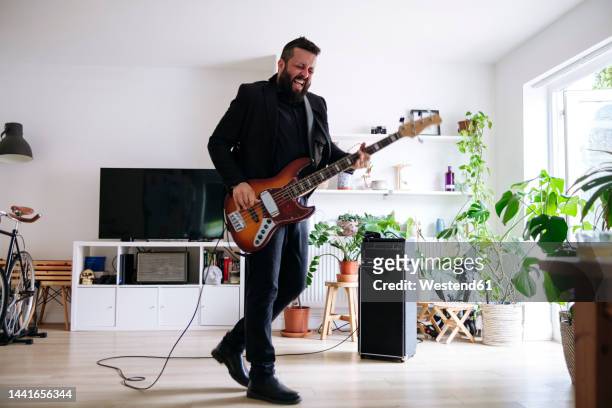 mature man playing electric guitar in living room at home - electric guitar stock-fotos und bilder
