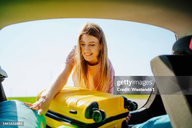 happy girl loading yellow suitcase in car trunk - yellow suitcase stock pictures, royalty-free photos & images