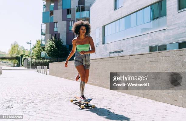 young woman longboard skating outside building on sunny day - woman longboard stock-fotos und bilder