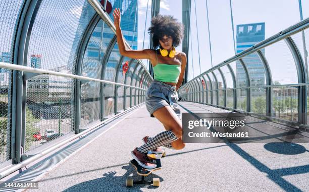 woman with hand raised longboard dancing on bridge - woman longboard stock-fotos und bilder