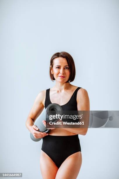 smiling mature woman holding gray exercise mat against white background - body conscious stock pictures, royalty-free photos & images