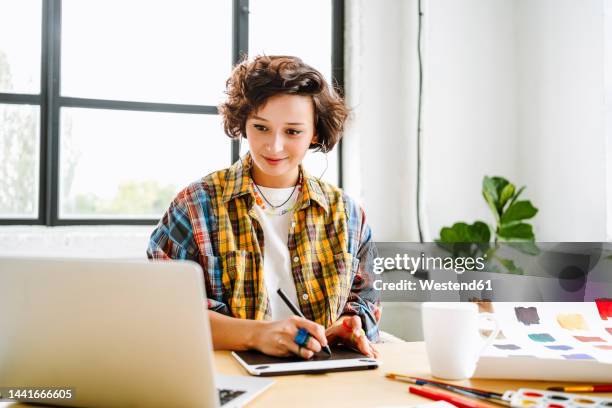 smiling illustrator with graphics tablet using laptop at office - ilustrador fotografías e imágenes de stock