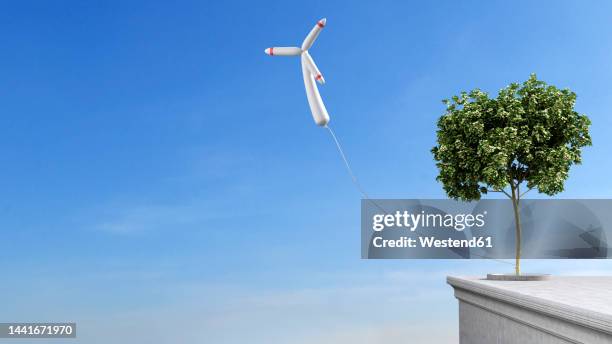 wind turbine shaped balloon tied to single tree growing on rooftop - at the edge of stock illustrations