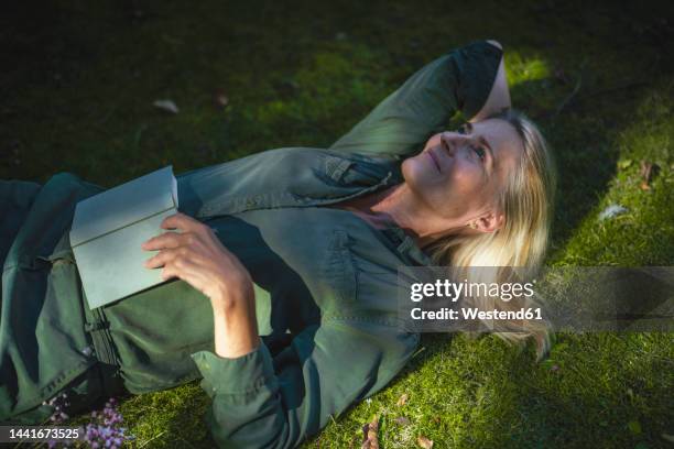 contemplative woman lying on grass in garden - lying on grass stock-fotos und bilder