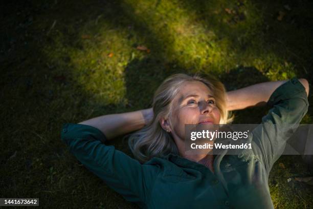 thoughtful mature woman lying on grass in garden - beautiful blonde babes stock pictures, royalty-free photos & images