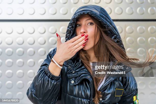 woman covering mouth with hand in front of metal wall - padded jacket 個照片及圖片檔