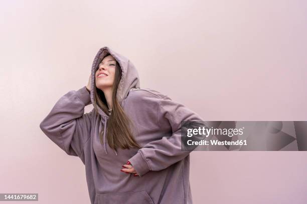 woman with eyes closed dancing in front of pink wall - hoodie stock pictures, royalty-free photos & images