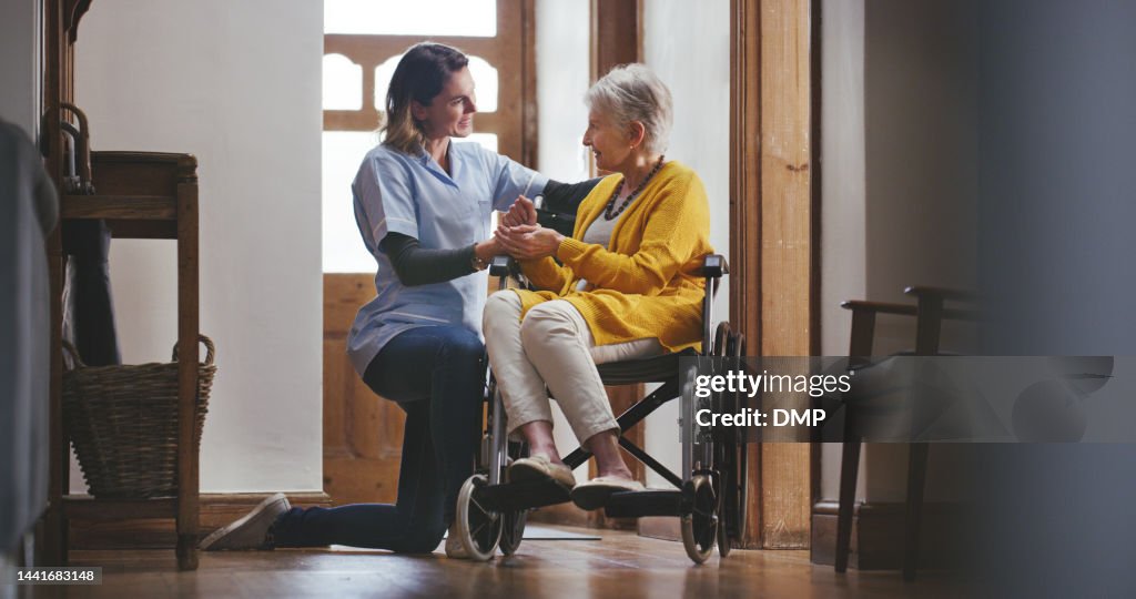 Disability, caregiver and old woman in a wheelchair in a house helping a disabled elderly patient with alzheimers. Retirement, nurse and healthcare social worker holding hands and talking to a senior