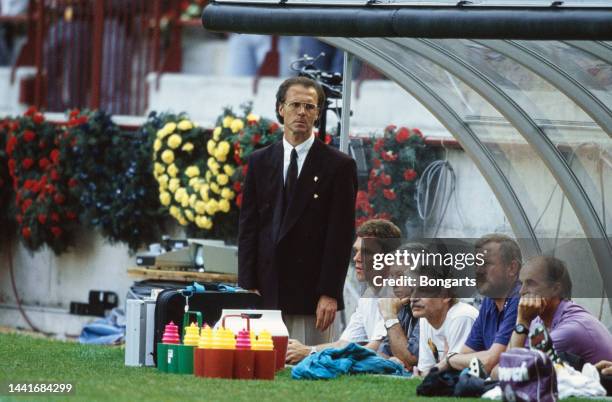 German football manager and former footballer Franz Beckenbauer, manager of the West Germany national team, standing in the dugout, with his...