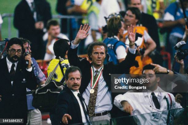 German football manager and former footballer Franz Beckenbauer is crowded by photographers, his winner's medal around his neck, among people...
