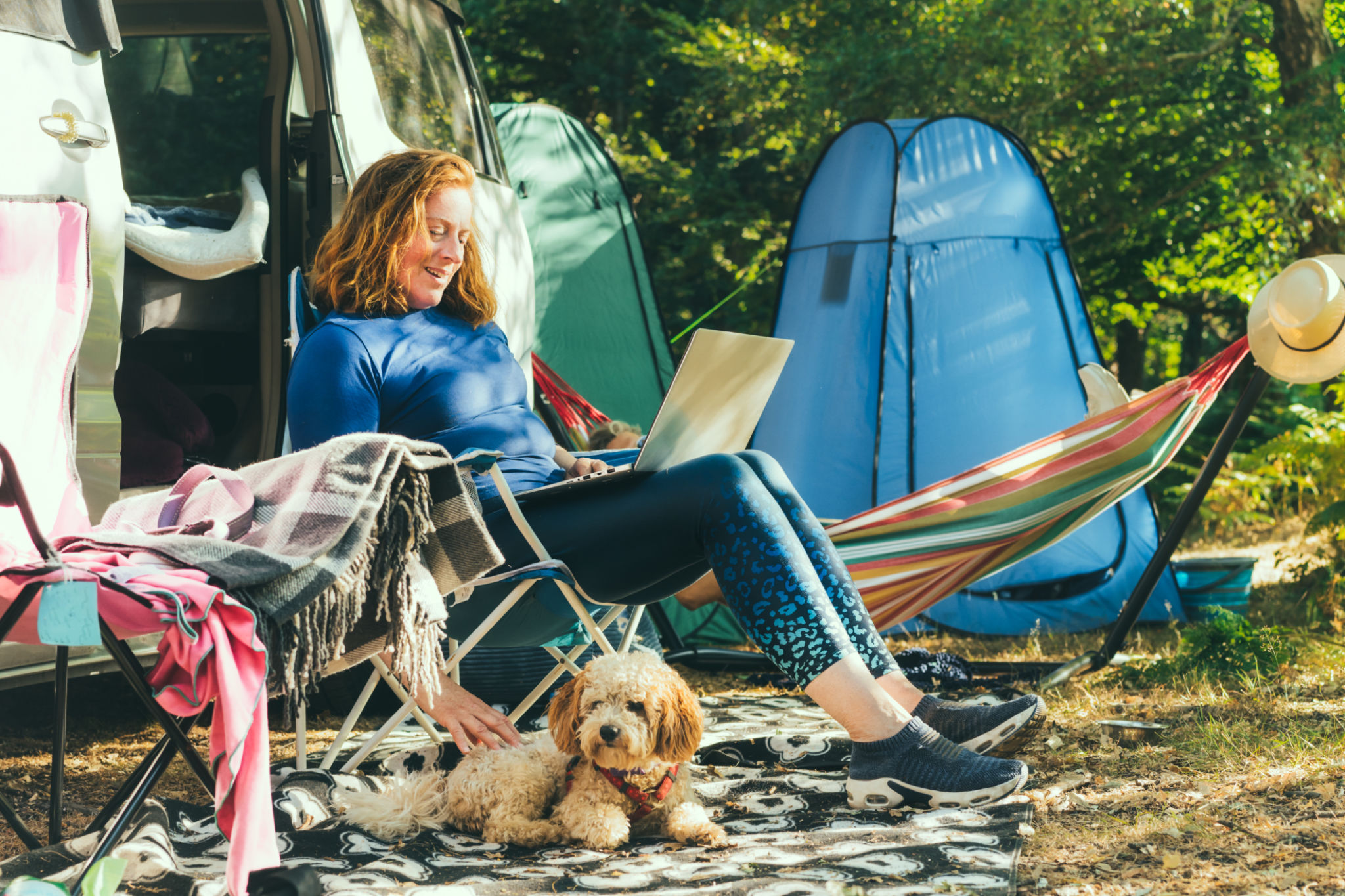 Adult woman working on laptop, sitting in the travel chair with her cockapoo puppy on the background of camper car vehicle. Female living on a motorhome with animals and travel the world. Best friend. Adult woman working on laptop, sitting in the travel chair with her cockapoo puppy on the background of camper car vehicle. Female living on a motorhome with animals and travel the world. Best friend.