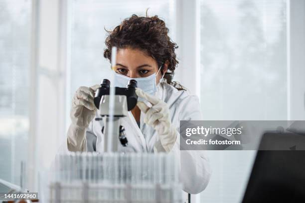 portrait of focused female scienitst analyzing a sample under a microscope - ecuadorian ethnicity stock pictures, royalty-free photos & images