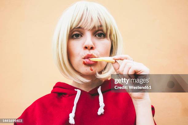 woman eating french fries in front of peach wall - burger portrait stock-fotos und bilder