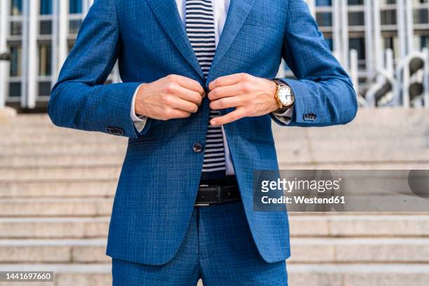 businessman buttoning suit jacket in front of staircase at office park - abrochar fotografías e imágenes de stock