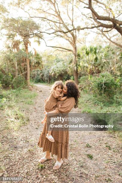 eine 31-jährige kubanische mutter mit ihrer 3-jährigen tochter in passenden goldbraunen kleidern in einem waldreichen wald in südflorida im november 2022 für ein gemütliches herbst-mutter/tochter-porträt - koordination stock-fotos und bilder