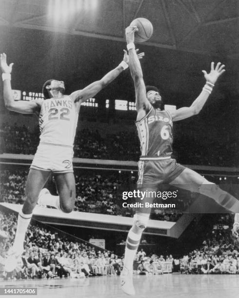 Hawks' John Drew and 76ers Julius Erving both get high of the hardwood fighting for a rebound during action.