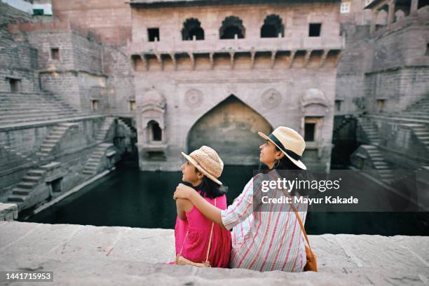 vista trasera de la madre y la hija turistas sentadas en el pozo del paso - historia social fotografías e imágenes de stock