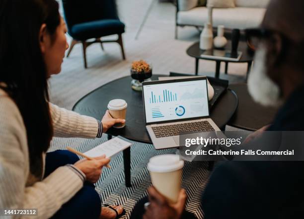 coworkers look at a laptop together as they drink takeaway coffees - estrategia de negocio fotografías e imágenes de stock