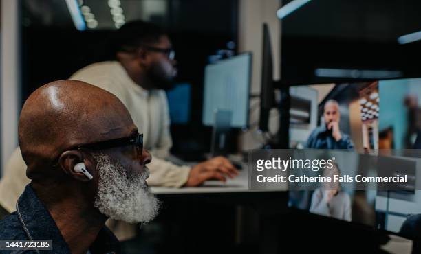 two men work late at the office. one takes a video conference call, while the other works at a standing desk. - zoom participant stock pictures, royalty-free photos & images