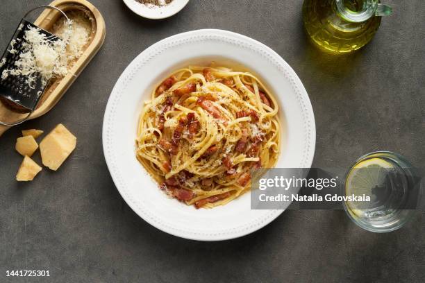 carbonara pasta. spaghetti with pancetta, egg, pepper,parmesan cheese and cream sauce. cheese grater, olive oil, glass of water on table. traditional italian cuisine. top view. - parmesan cheese overhead stock pictures, royalty-free photos & images