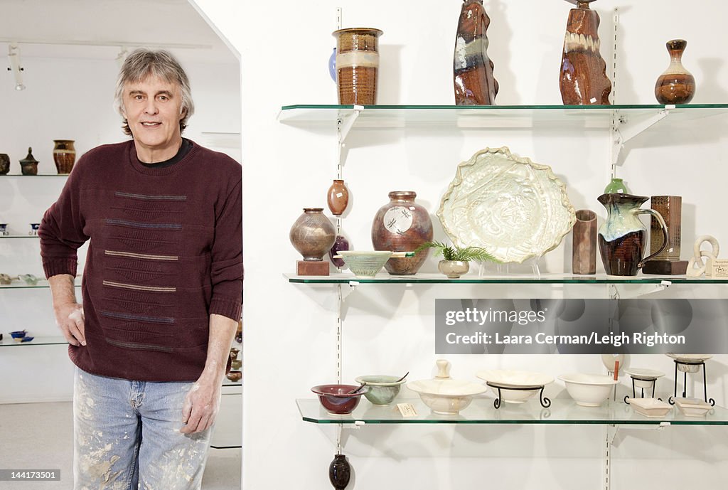 Potter standing in gallery with finished pieces.