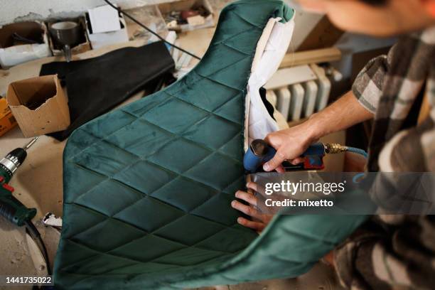 young upholstery worker applying fabric on a chair with a pneumatic stapler in the workshop - upholstery worker stock pictures, royalty-free photos & images