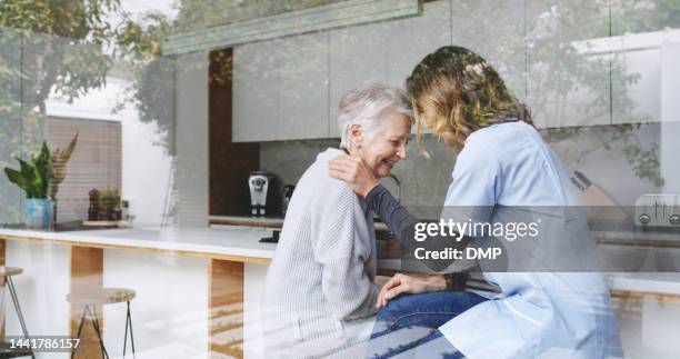 dolore, sostegno e infermiera con donna anziana in pensione seduta nella cucina della sua casa. triste, aiuto e operatore sanitario o caregiver confortare la signora anziana con simpatia in casa di cura. - ospizio foto e immagini stock