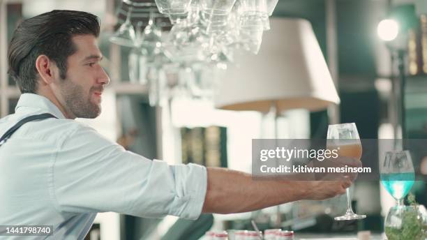 der junge barkeeper trägt eine schürze und bereitet sich auf die arbeit vor, indem er getränke an einer party- oder bartheke oder einem restaurant zubereitet, wobei viele leute kommen, um abzuhängen, zu reisen, zu reden, spaß zu haben und sich zu ents - candy bar stock-fotos und bilder