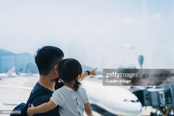 loving young asian father carrying cute little daughter in arms, looking at airplane through window at the airport terminal while waiting for departure. family travel and vacation. embark on a new journey with the family - toddler at airport stock-fotos und bilder