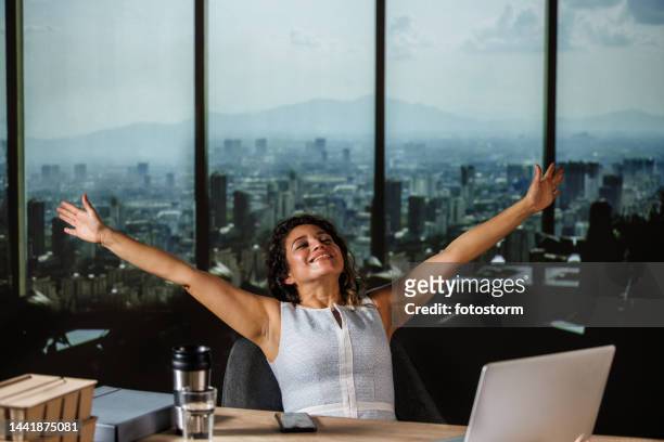 woman leaning back in her chair, eyes closed, arms outstreched, smiling and taking a breather after successfully finishing a work day - ecuadorian ethnicity stock pictures, royalty-free photos & images