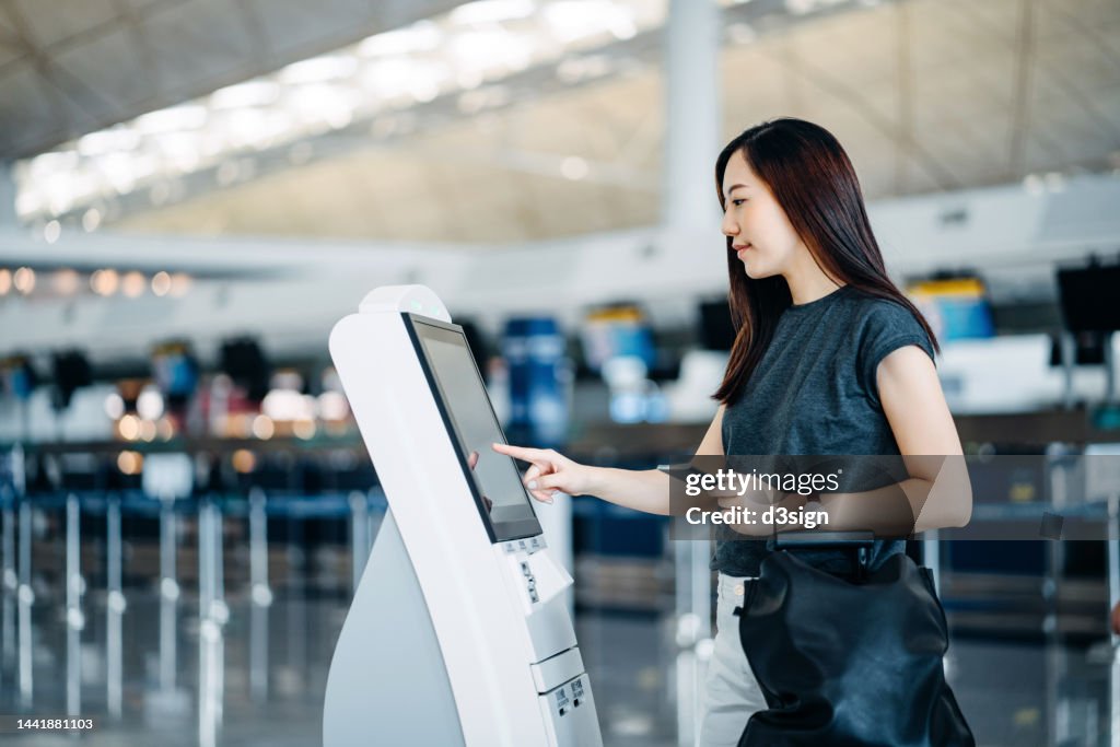 Young Asian woman travelling by plane, checking in at the airport using a self service check in machine. Ready to travel. Travel and vacation concept. Businesswoman on a business trip