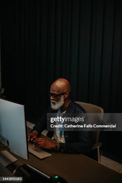 a man sitting behind a computer at a desk looks at his desktop pc - office 60s computer person in front of screen stock pictures, royalty-free photos & images