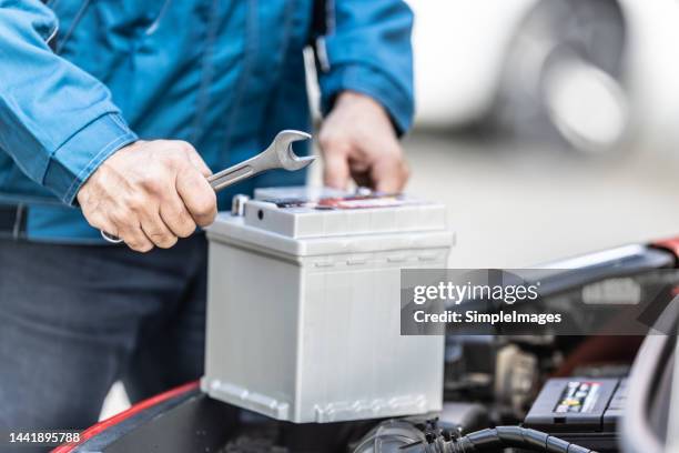 mechanic holds key over car battery with engine trunk of the car open. - car battery stockfoto's en -beelden