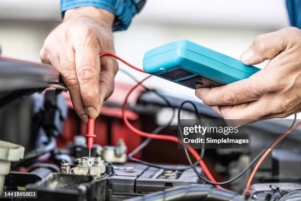 car electrician or mechanic checks voltage in car battery inside the car engine with open hood. - laying on car hood stock pictures, royalty-free photos & images