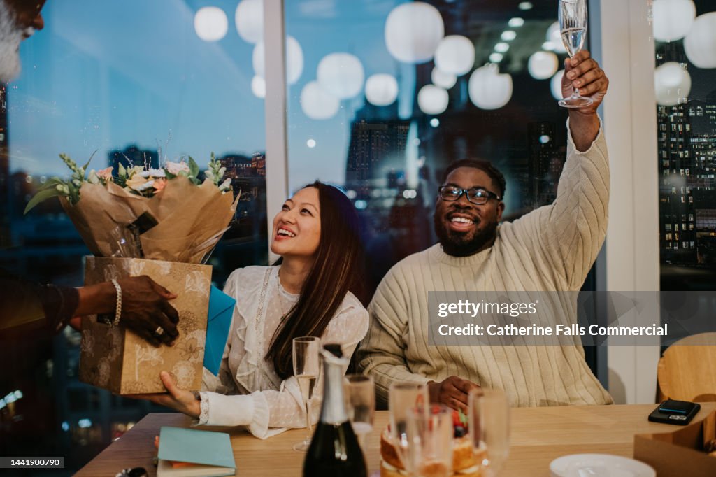 A happy woman is presented with a bouquet of flowers at an after-work office party