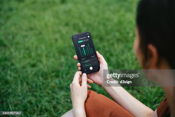 young asian woman using smart home energy monitor app on smartphone to check and manage the energy usage of her home outdoors. home energy monitor allows to monitor energy use and set energy budgets. energy control and efficiency management concept - adjusting bildbanksfoton och bilder