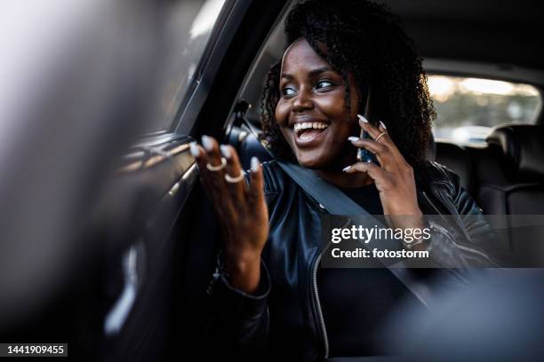 joyful young woman having a conversation with a friend on the phone while riding in the back seat of a taxi - car pooling stock pictures, royalty-free photos & images