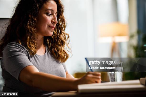 copy space shot of smiling woman sitting at her desk and writing a to do list in her planner - ecuadorian ethnicity stock pictures, royalty-free photos & images