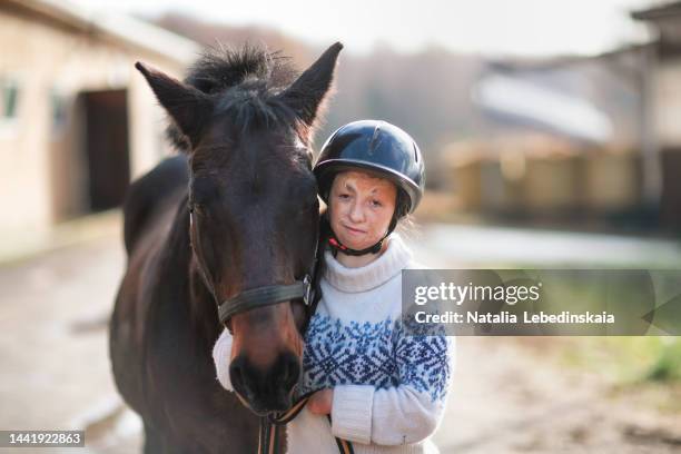 teenage girl in riding helmet and pullover hugs dark horse. outdoors. - showus fitness stock pictures, royalty-free photos & images