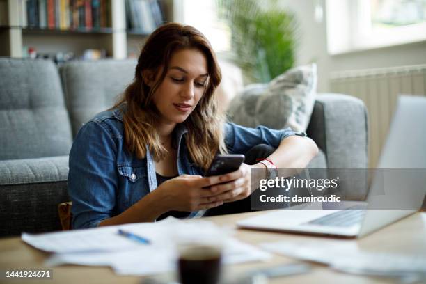 young smiling woman using mobile phone while studying at home - woman texting on cell phone stock pictures, royalty-free photos & images