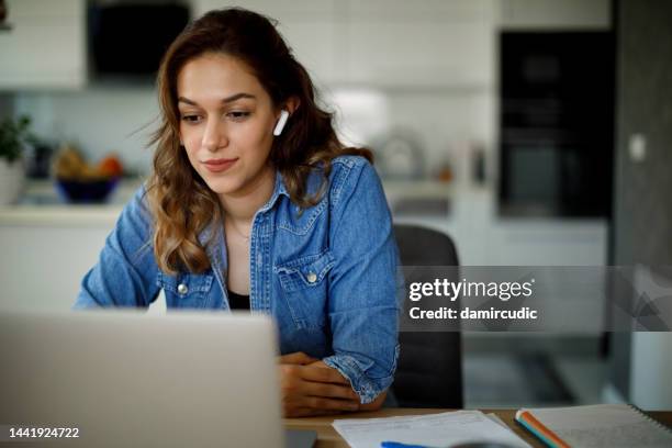 smiling young woman with bluetooth headphones attends an online course at home - in ear headphones stock pictures, royalty-free photos & images