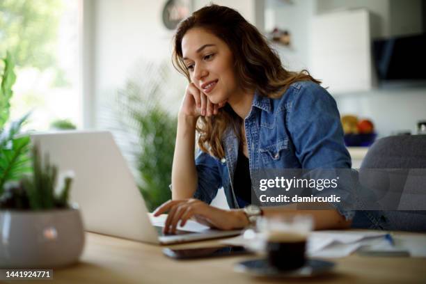 smiling young woman following online courses on her laptop at home - tutorial stockfoto's en -beelden