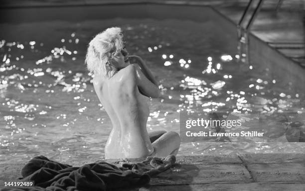 American actress Marilyn Monroe looks over her shoulder as she sits topless on the deck of a pool during the filming of 'Something's Got to Give' ,...