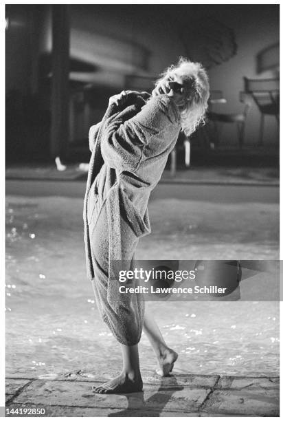 American actress Marilyn Monroe , naked, tilts her head back as she pulls on a blue bathrobe on the deck of a pool during the filming of 'Something's...